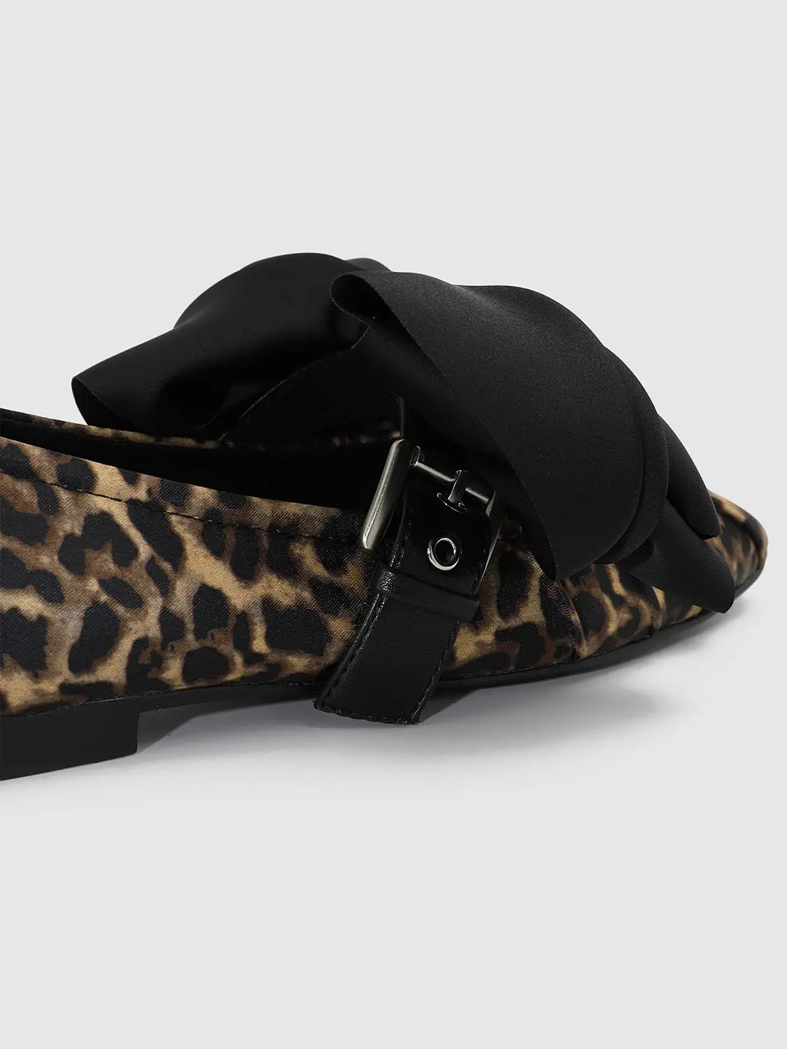 Flats with leopard print fabric, black bow accent, and buckle strap