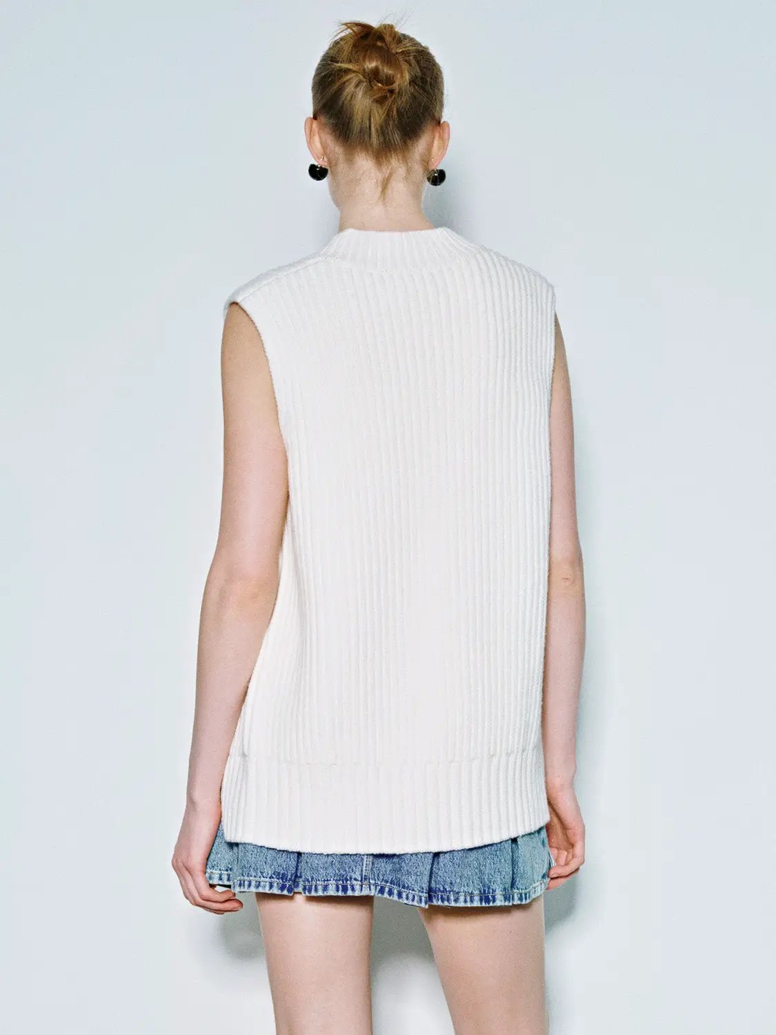 Loose white rib-knit vest worn by model with denim shorts; back view