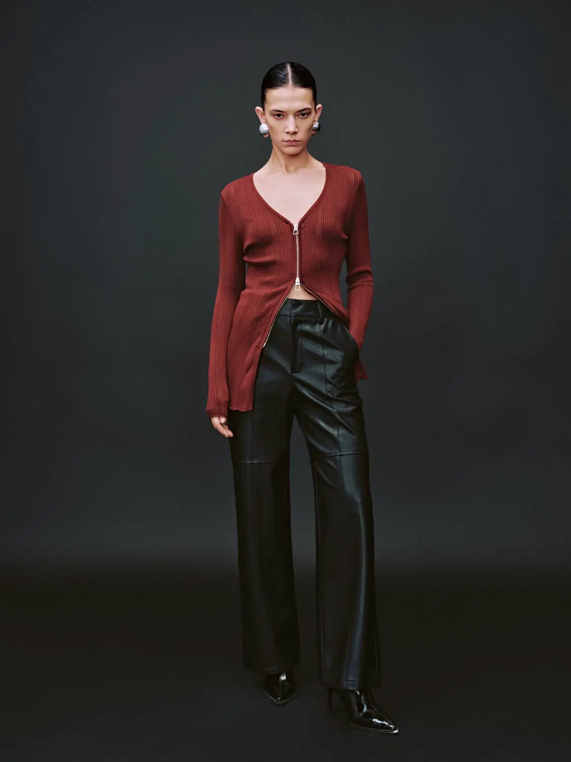 Zip-up front knitted cardigan in burgundy with a silver zipper; long sleeves worn by model with black leather pants.
