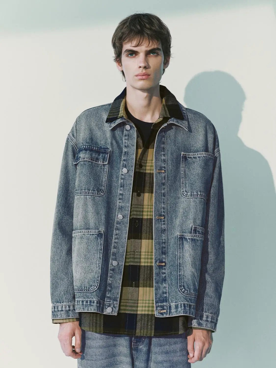 Denim jacket in blue stonewash with chest and lower pockets, layered over a green plaid shirt