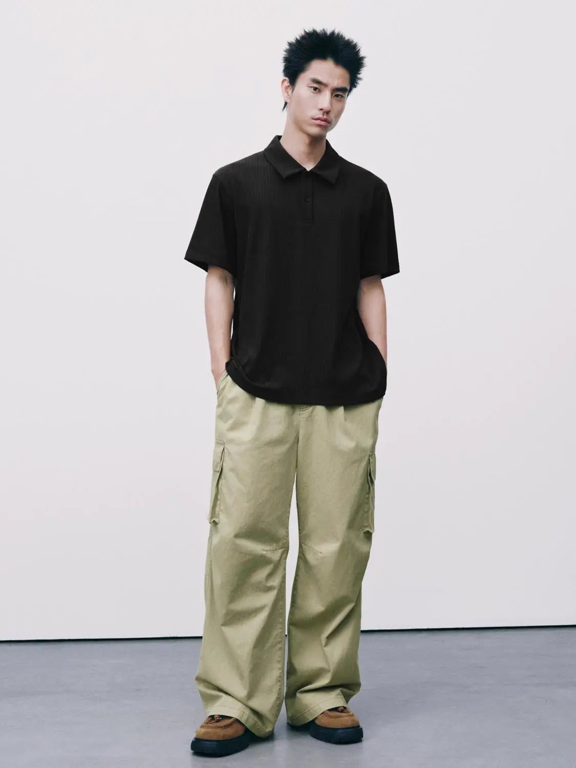Polo shirt in black, short-sleeve, worn by male model in beige cargo pants.