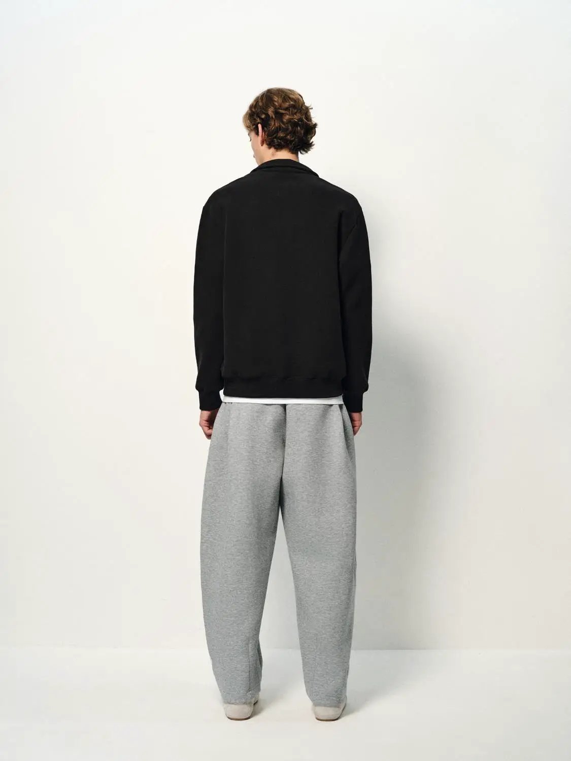 Sweatshirt in black on model, back view; gray sweatpants visible.