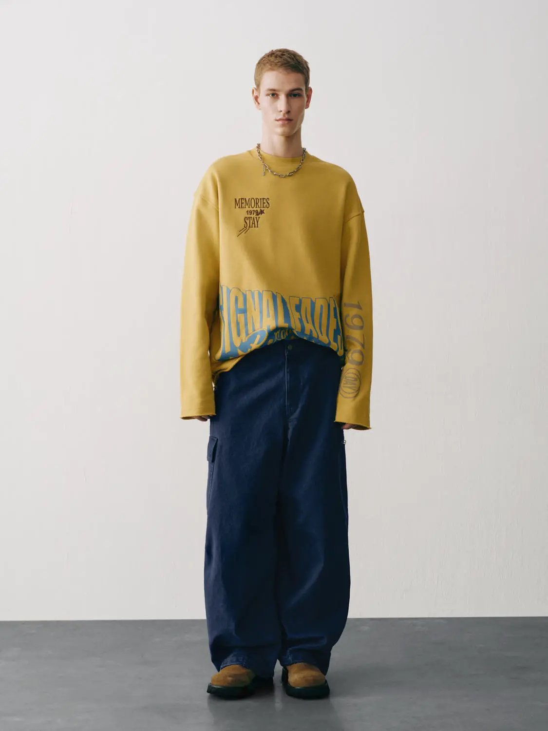 Sweatshirt in mustard yellow, oversized with bold blue graphic print, paired with navy cargo pants.