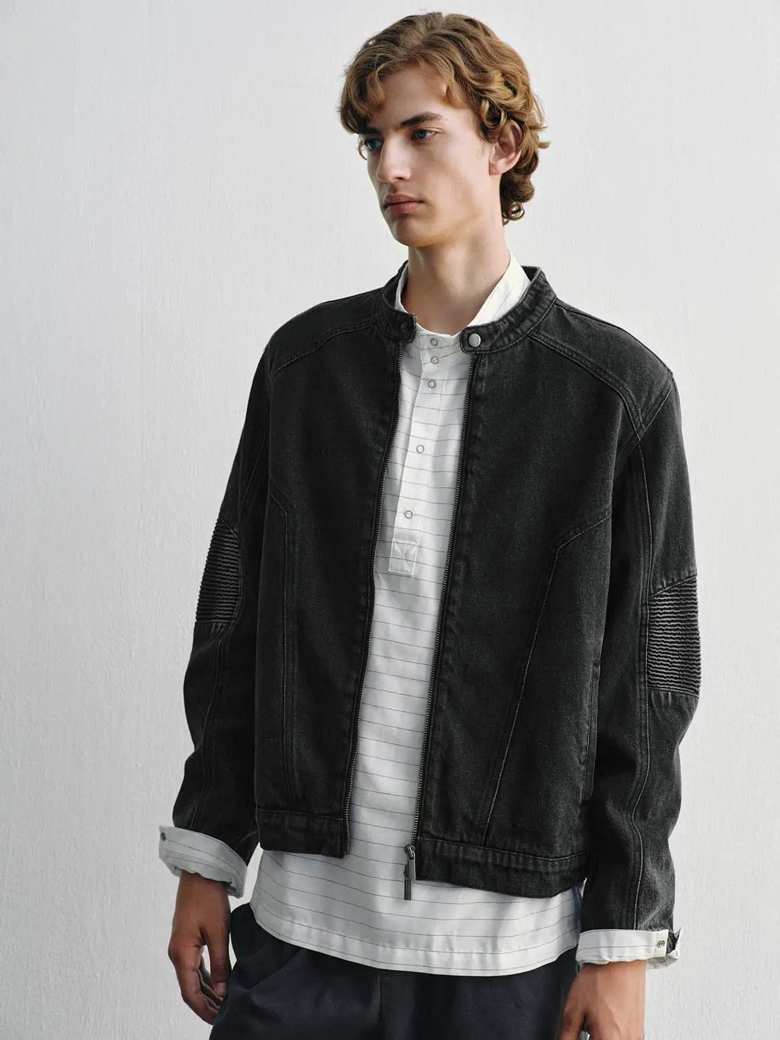 Denim jacket in black wash with zip front and ribbed sleeve panels over a white striped shirt.