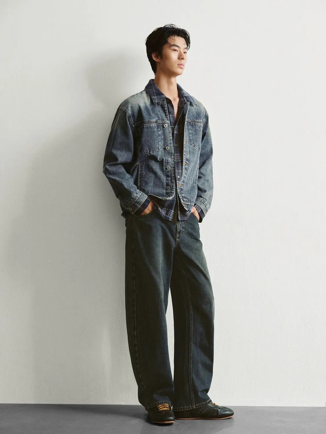 Faded blue denim jacket with a collar, metal buttons and front pockets worn over a plaid shirt.