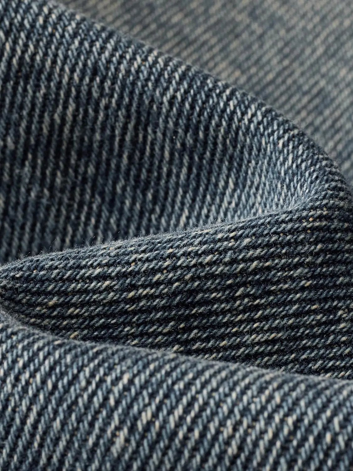 Denim jacket fabric close-up in faded blue tones, showing textured cotton denim