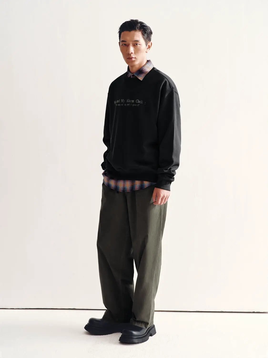 Sweatshirt by Urban Revivo Fashion in black, layered over plaid shirt with olive trousers.