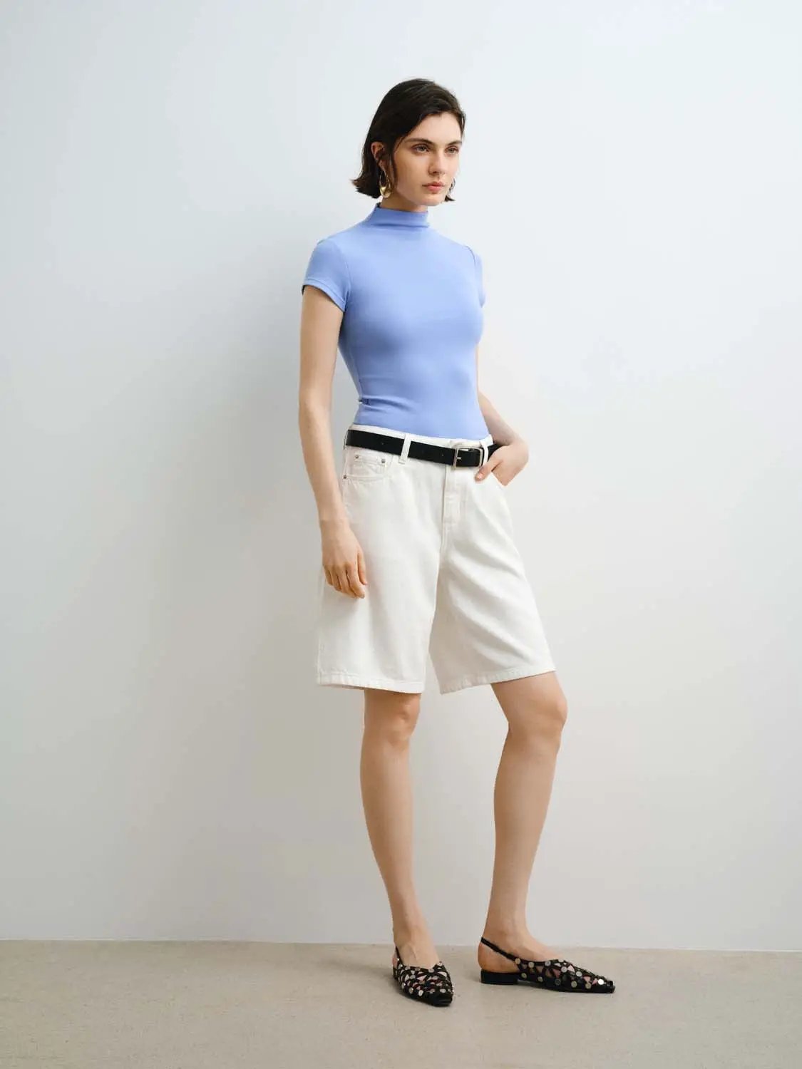 Women's modal knit T-shirt in light blue with a high neckline, fitted silhouette, paired with white shorts and a black belt.