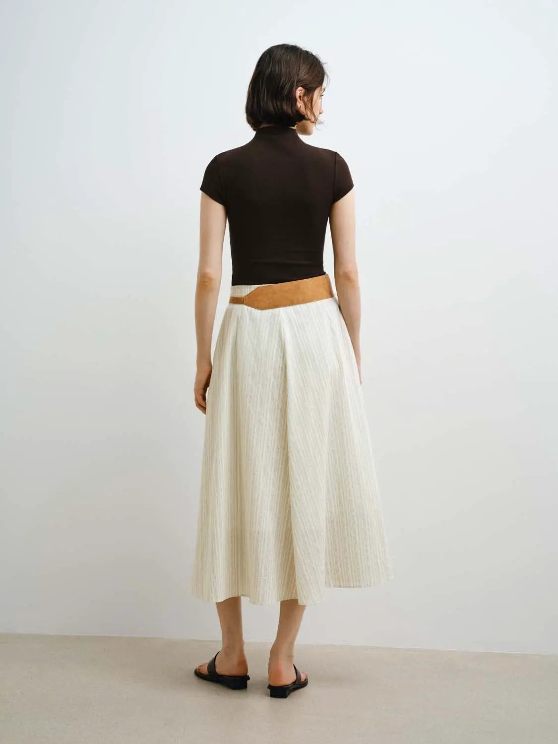 Women's black modal-knit T-shirt with cream pleated midi skirt and tan belt, two-piece back view