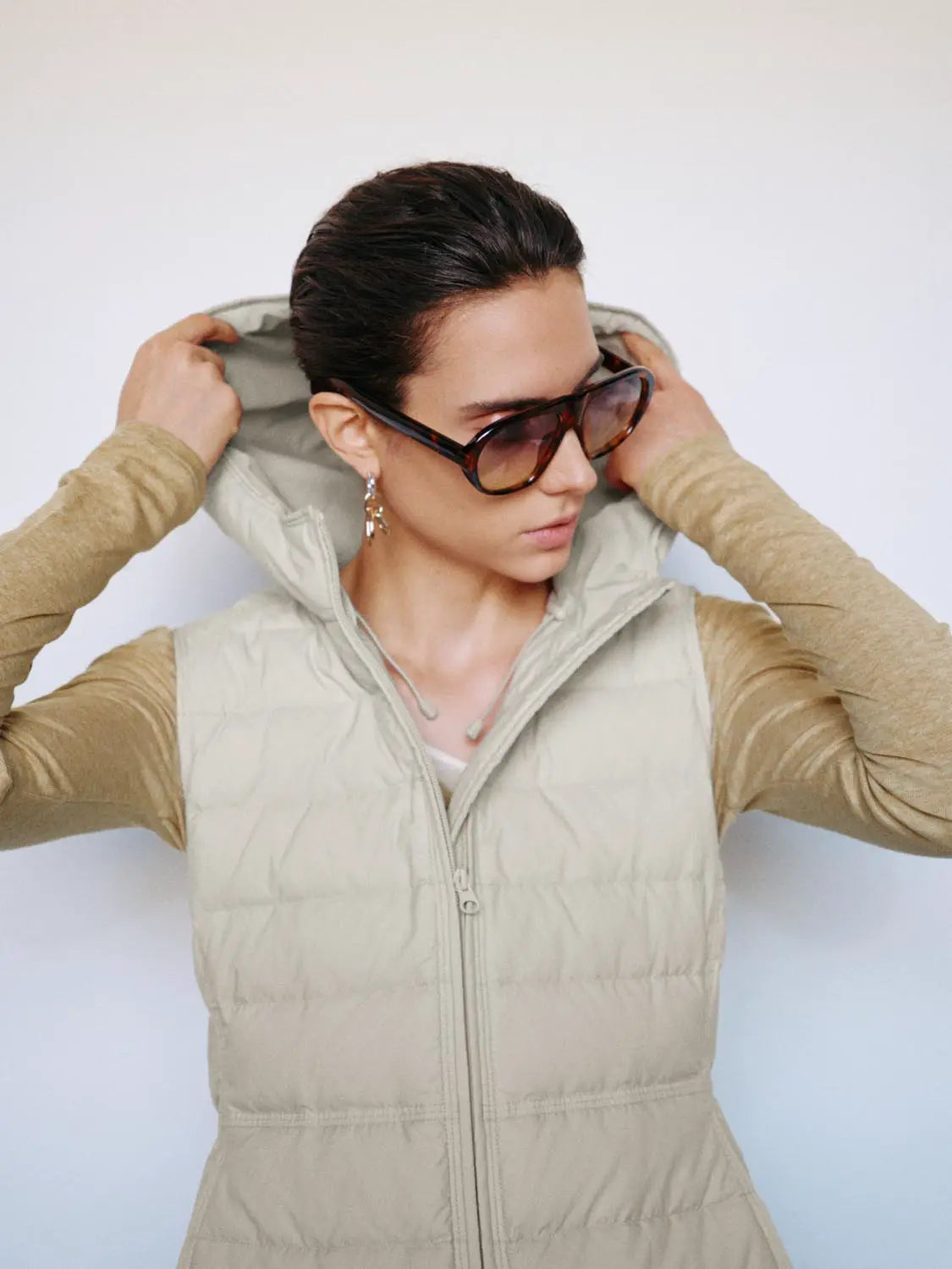 Down jacket with hood in cream beige, quilted puffer with front zipper, stylishly worn by a fashion model.