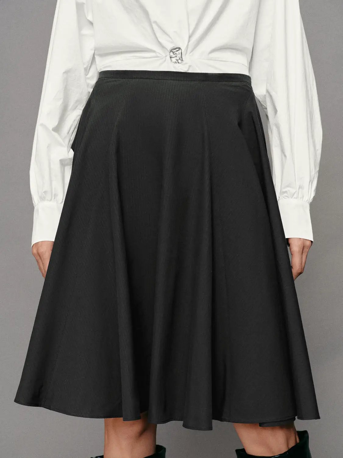 Pleated high-waisted cotton A-line skirt in black, shown with a white blouse on a fashion model for a polished look