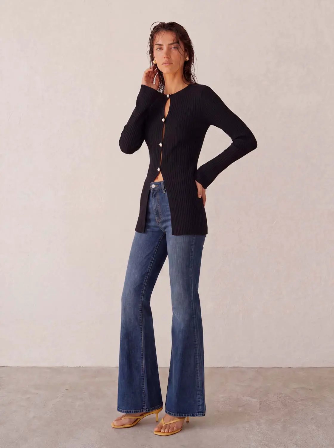 Skinny knitted cardigan in black ribbed knit with pearl buttons, worn with blue jeans.