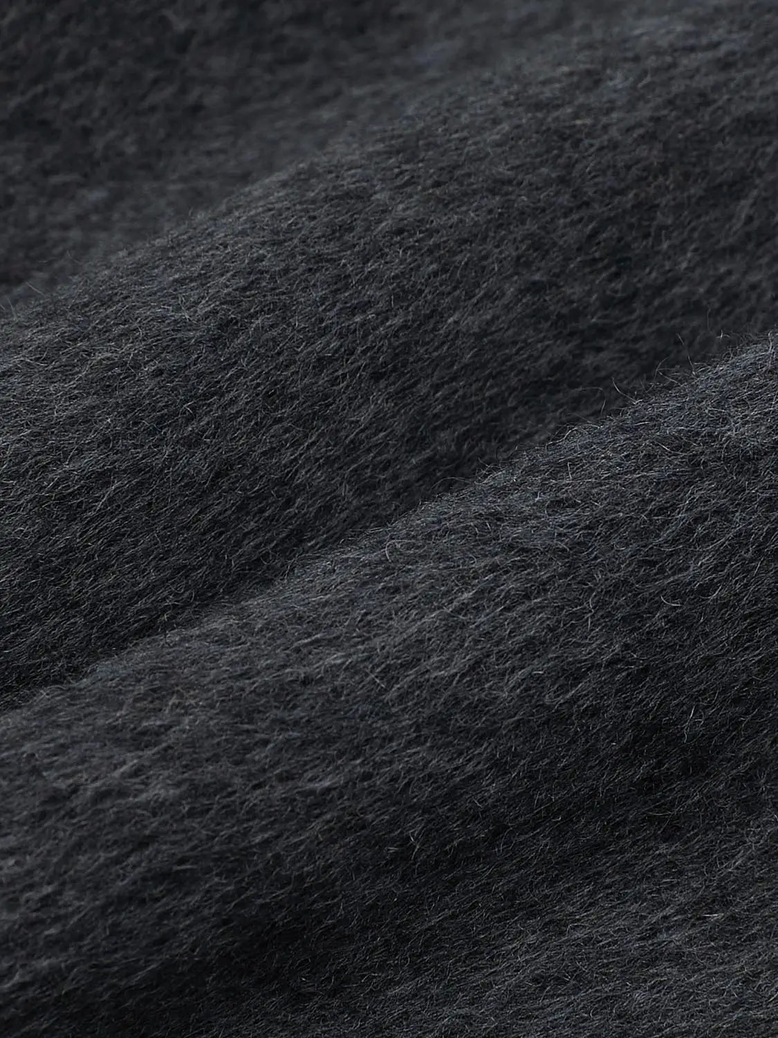 Coat fabric close-up in dark charcoal wool; plush, soft texture with visible fuzzy fibers and dense weave.