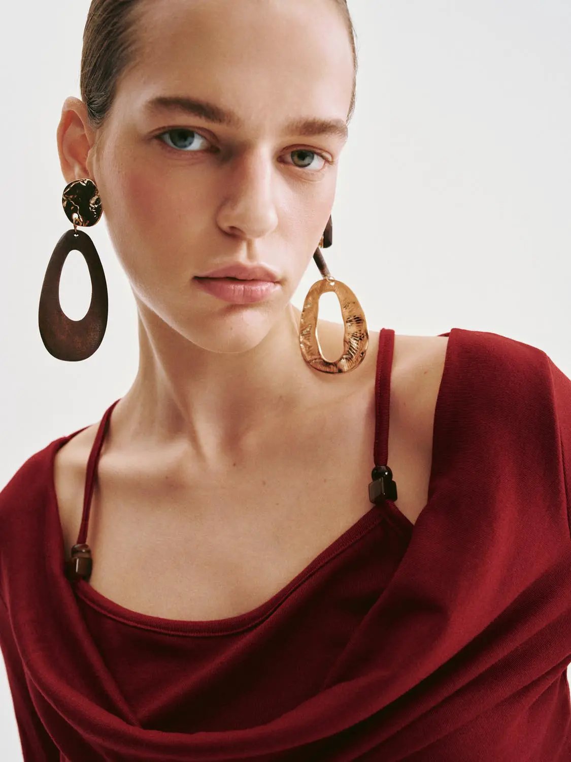 T-shirt in burgundy with draped neckline, model wearing oversized copper hoop earrings