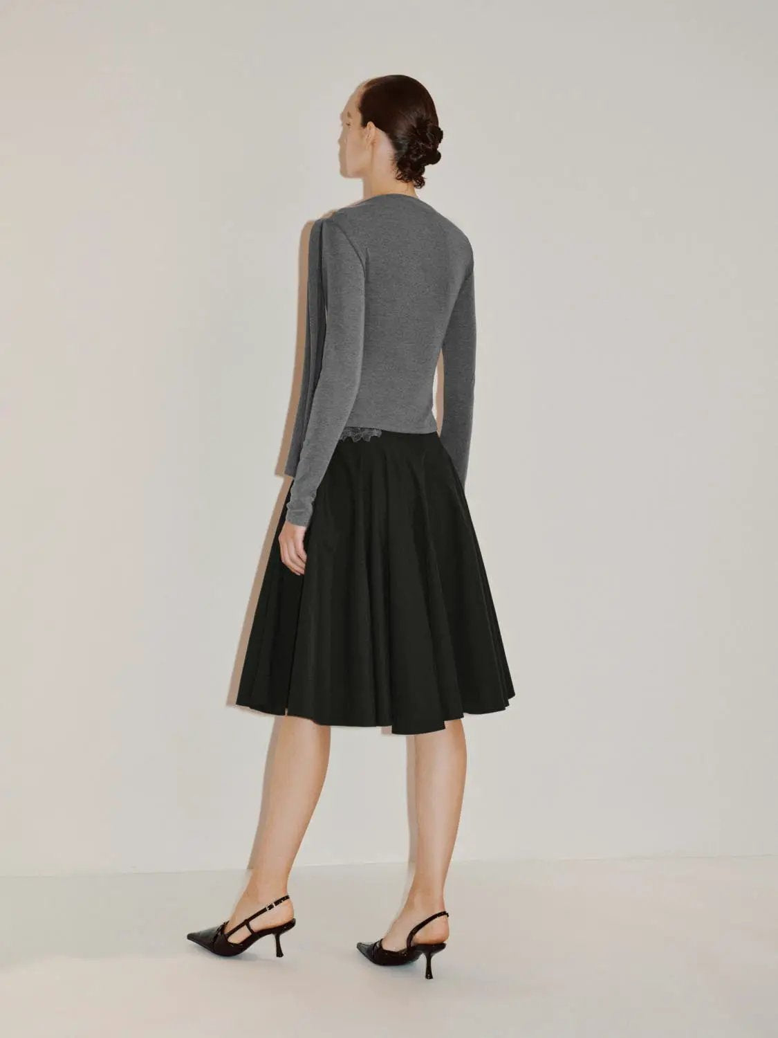 Draped one-shoulder grey long-sleeve blouse; shown with a black skirt.