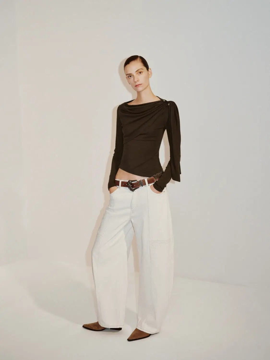 Draped one-shoulder long-sleeve black blouse; styled with white wide-leg pants.