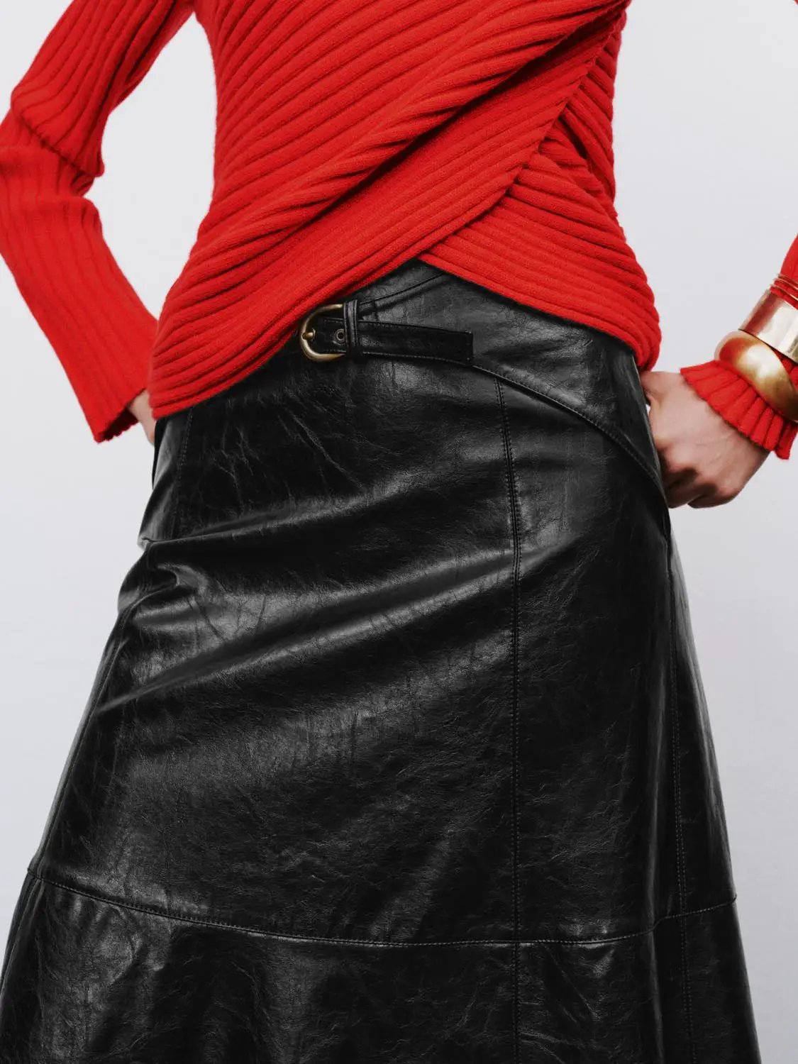 A-line black leather skirt with a metal waist belt buckle detail, paired with a red knit top