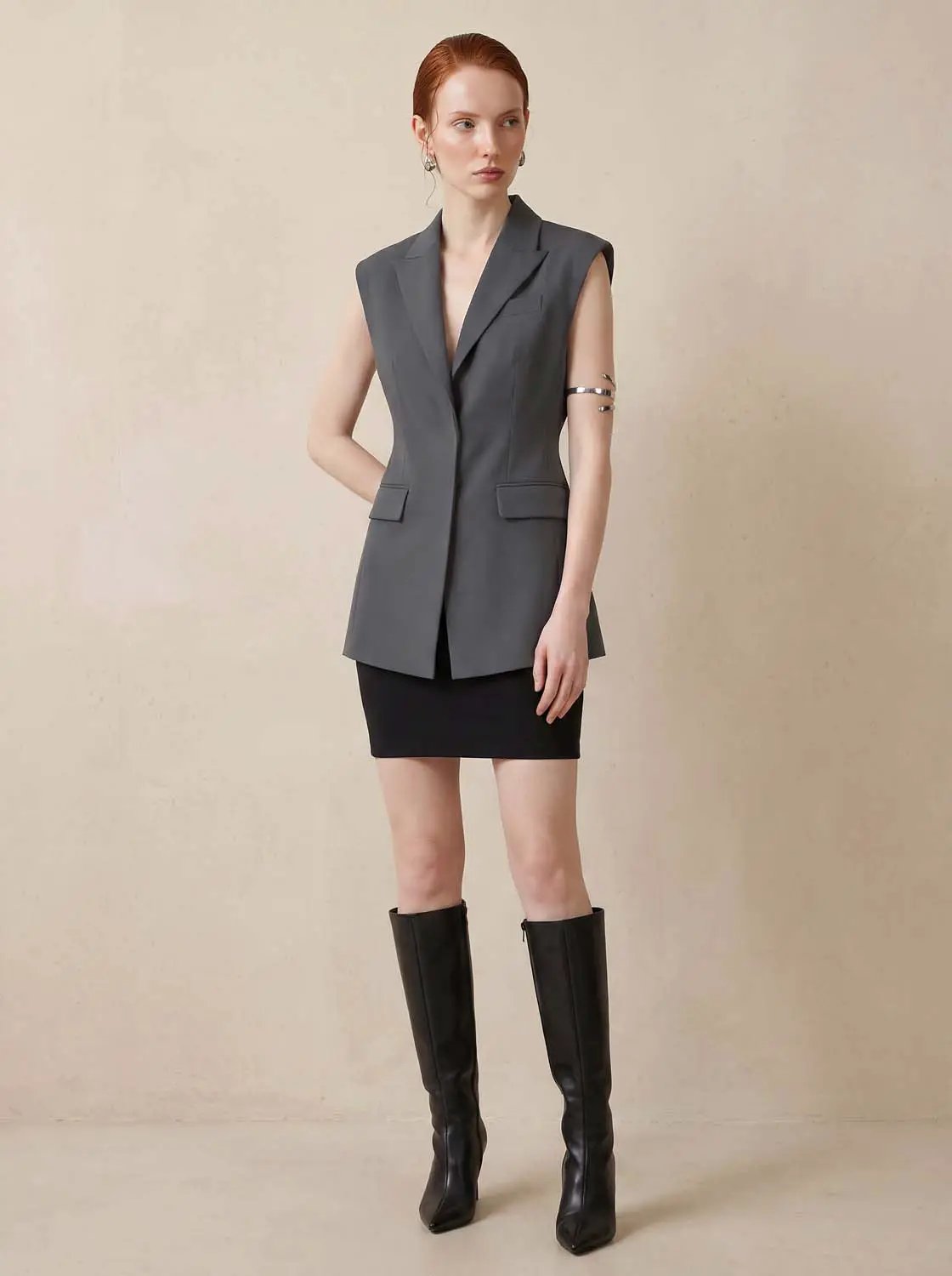 Sleeveless lapel-collar vest in charcoal gray with front buttons, styled with a black mini skirt