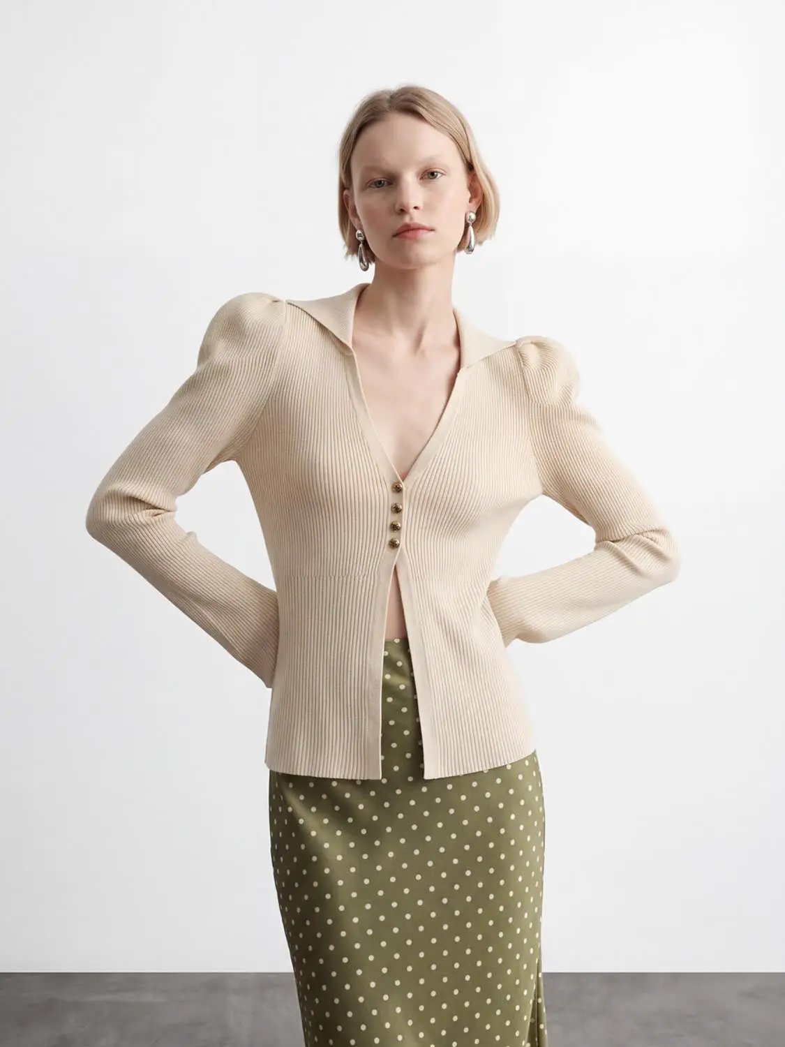 Puff Shoulder Tailored Knitted Cardigan in beige with ribbed texture and front buttons, paired with a polka-dot skirt.