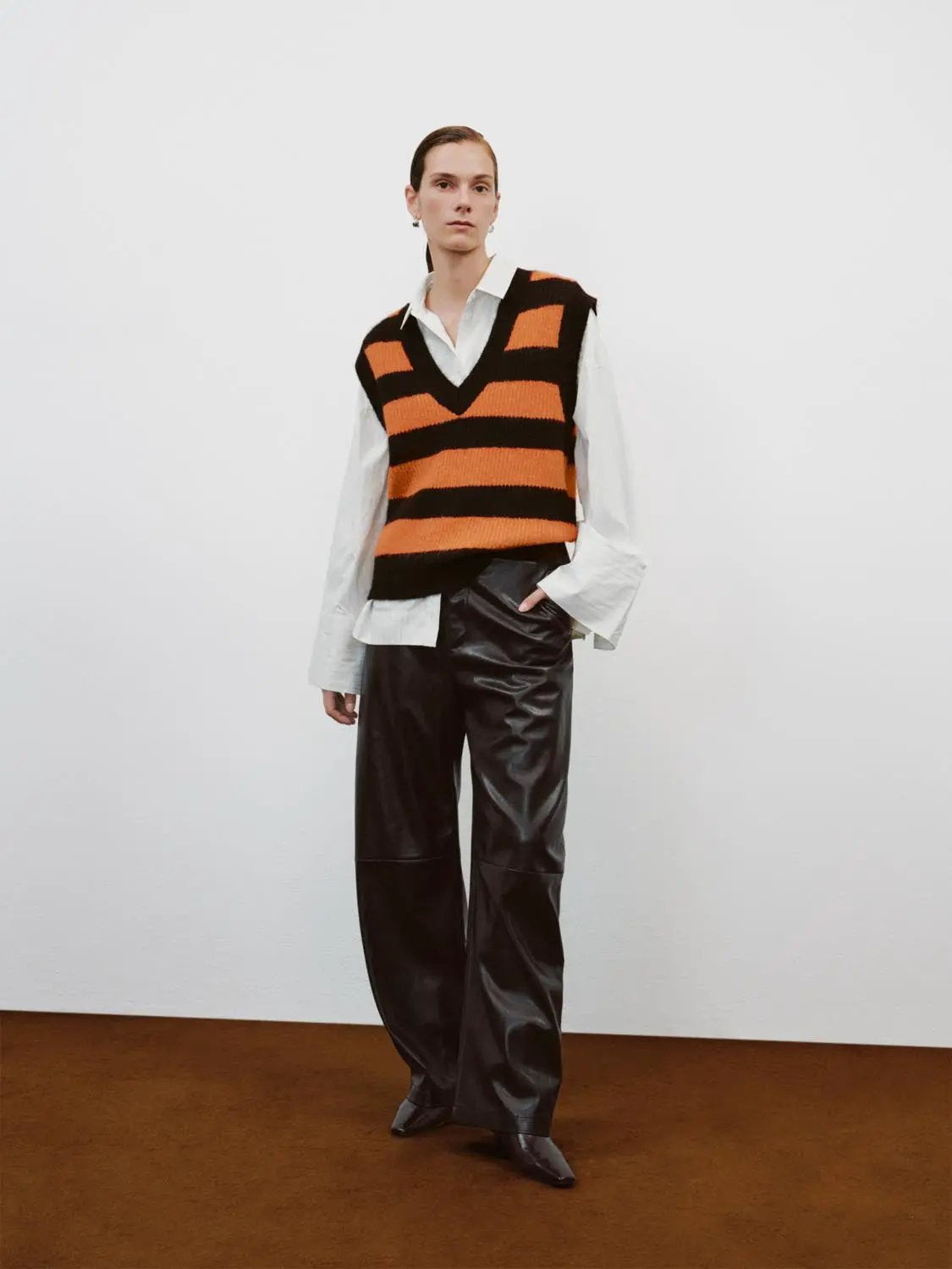 Striped stretch V-neck sleeveless knit tank top in orange and black, layered over white shirt and black wide-leg pants.