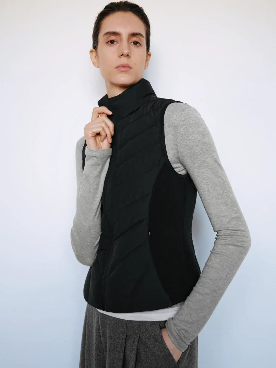 Down jacket vest, black quilted sleeveless style worn over a gray long-sleeve top