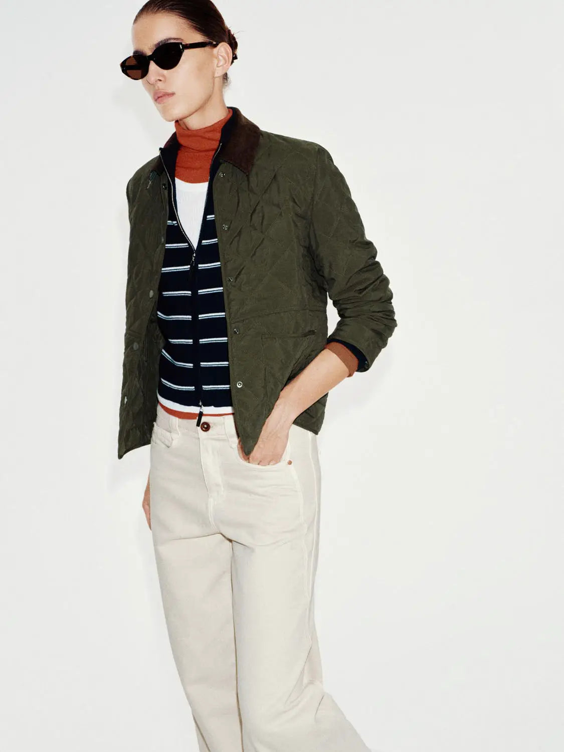Padded jacket olive green quilted with brown collar, worn by a model in a navy striped layer and orange turtleneck.
