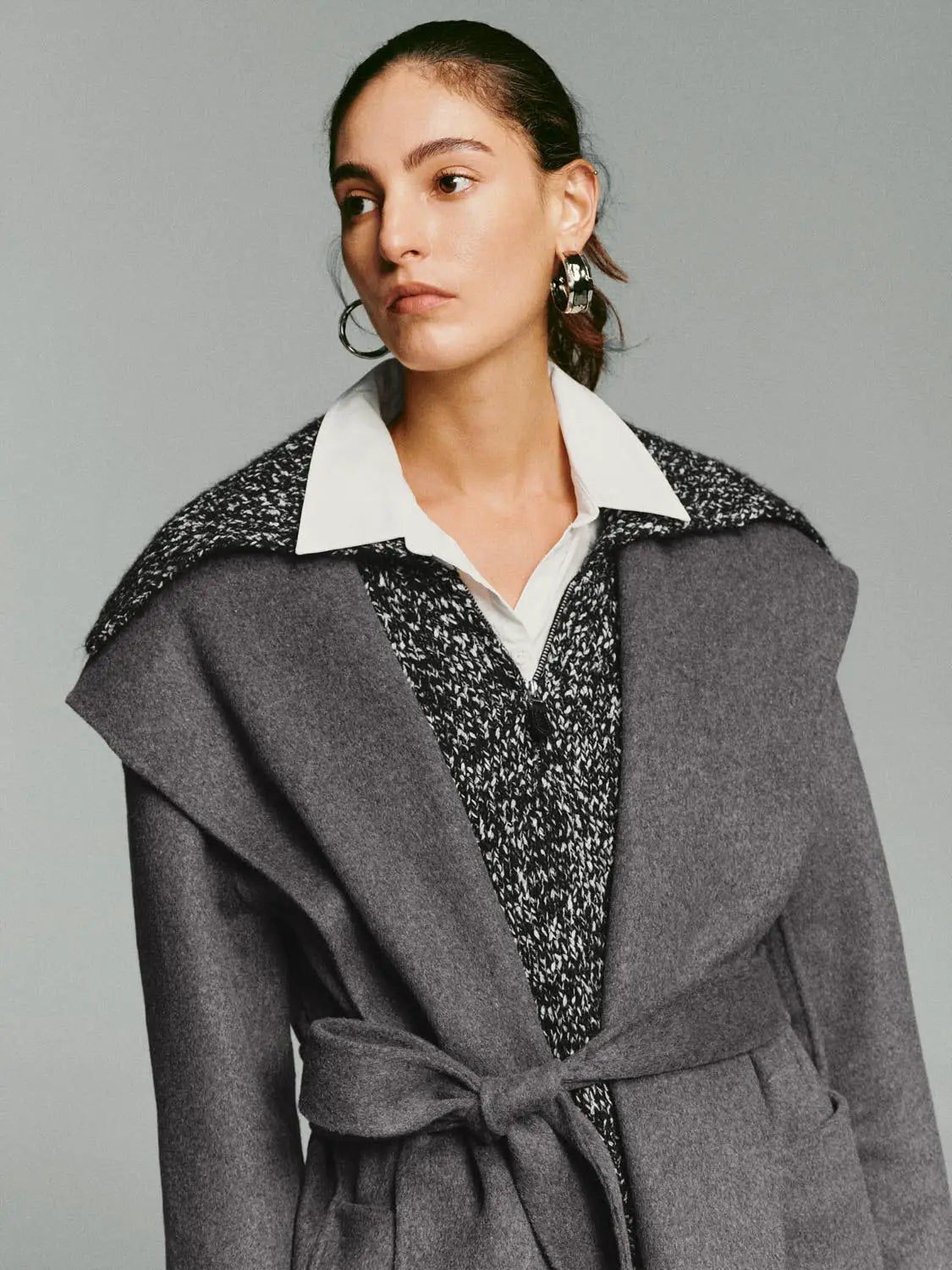 Grey wool coat with wide lapels and a belted waist, worn over a white-collared shirt.