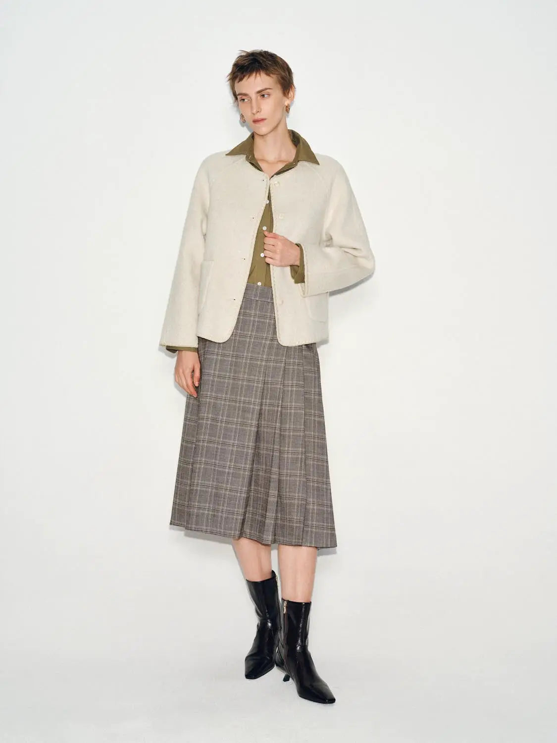 Coat, cream wool-blend with large front pockets; worn over an olive shirt and plaid midi skirt.
