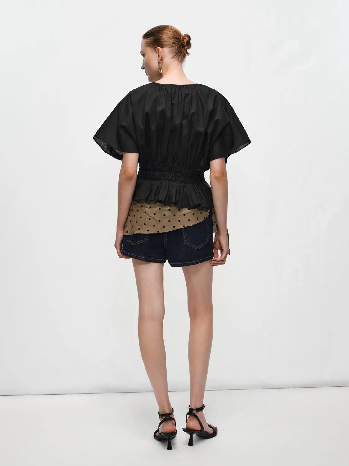 V-neck puff-sleeve blouse with smocked waist in black cotton-linen blend, paired with denim shorts