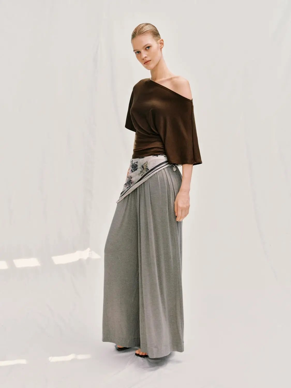 Draped short-sleeve ruched-waist T-shirt in brown, shown on a model with gray wide-leg pants