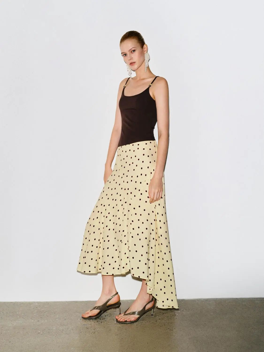 Polka-dot asymmetric-hem maxi wrap skirt in beige with dark spots, paired with a black tank top.