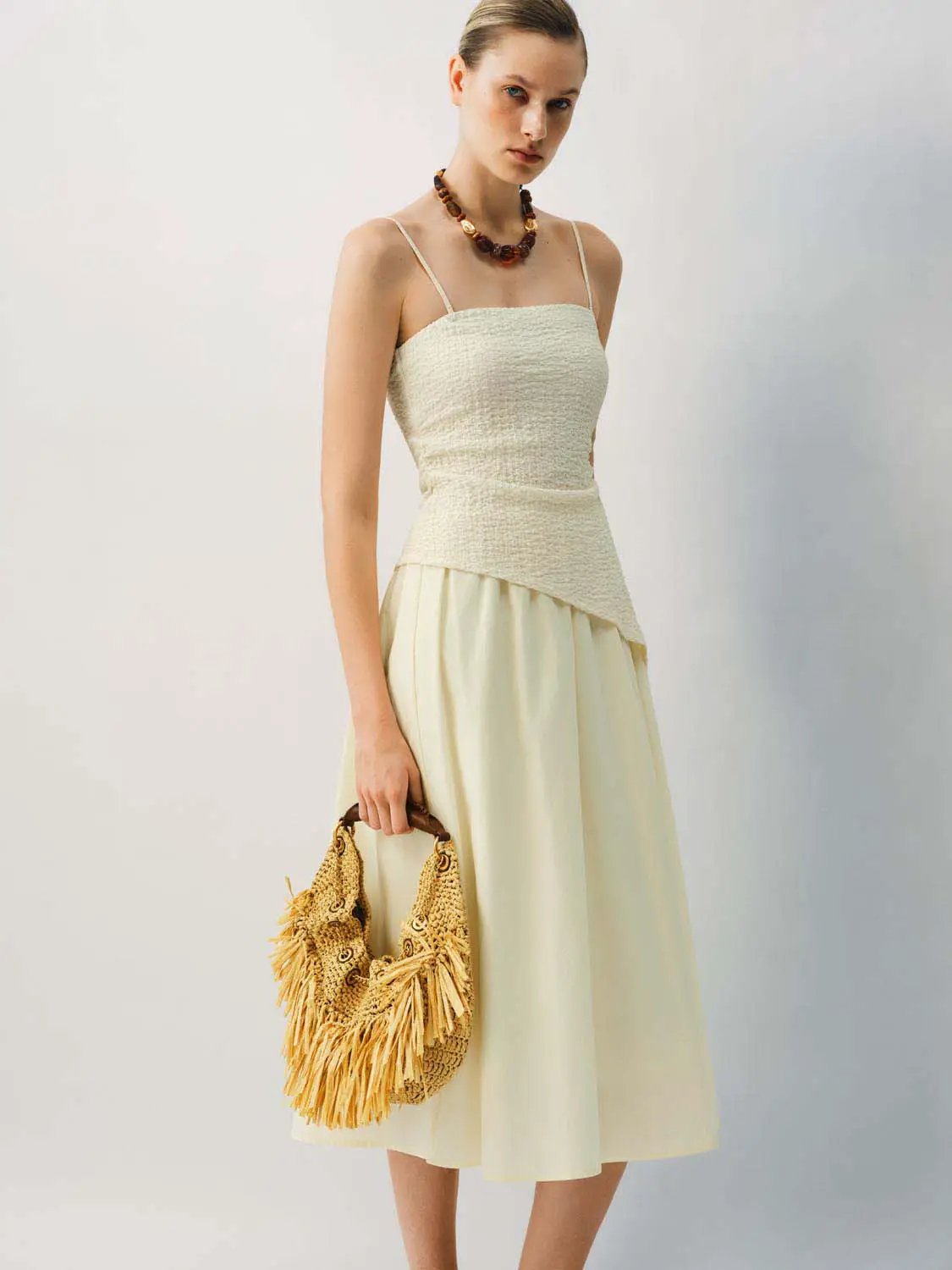 Thin Stretch Fabric Strappy A-Line Midi Dress in ivory with spaghetti straps, model carries a woven straw bag.