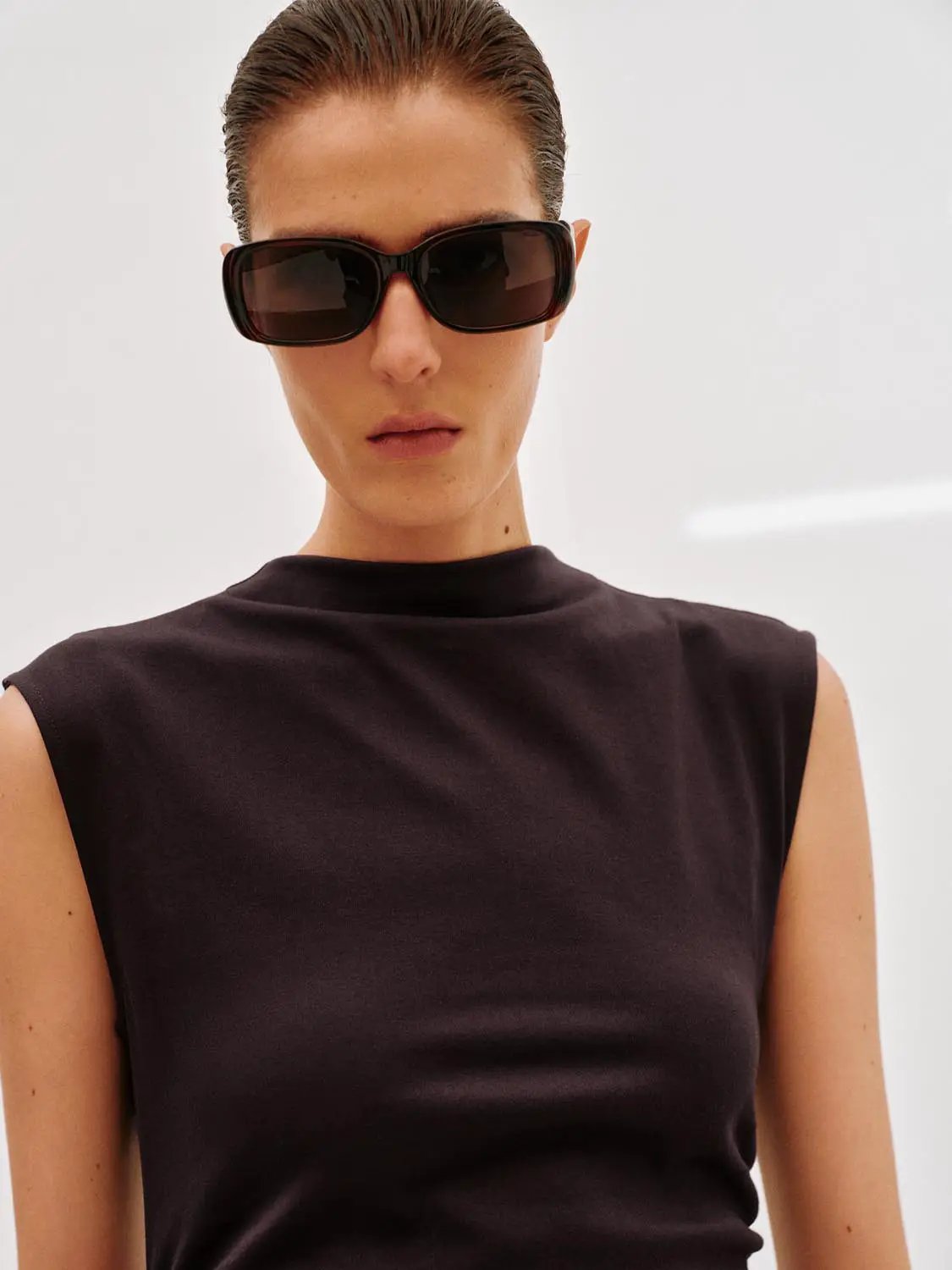 Dress, black sleeveless A-line style worn by model with oversized sunglasses