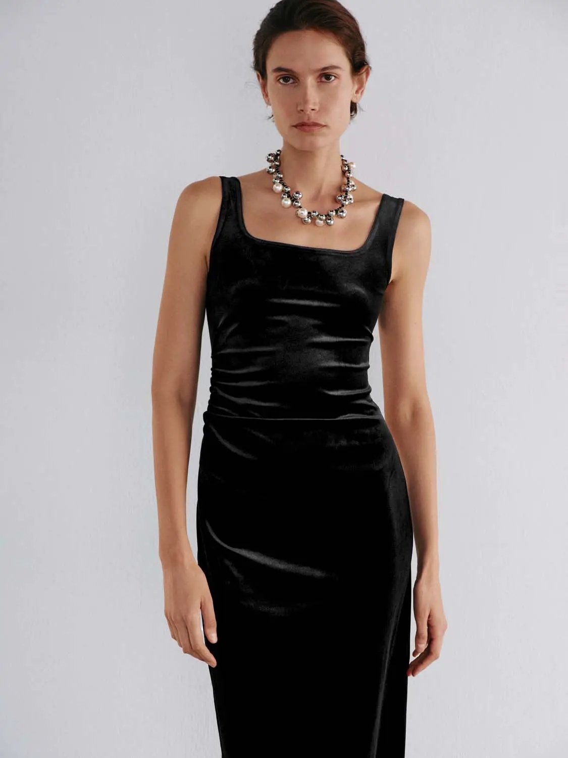 Ruched straight square neck sleeveless black velvet midi dress; model wearing a chunky pearl necklace.