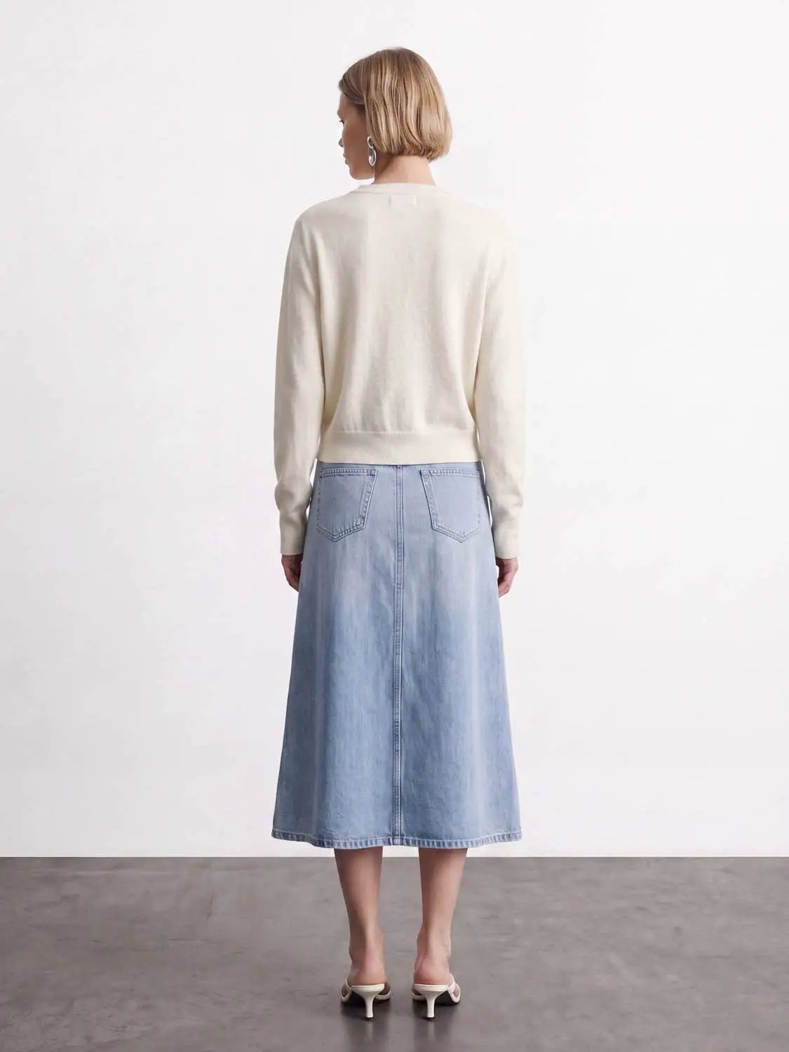 Knitted cardigan in ivory paired with light-wash denim midi skirt; back view of a two-piece outfit.
