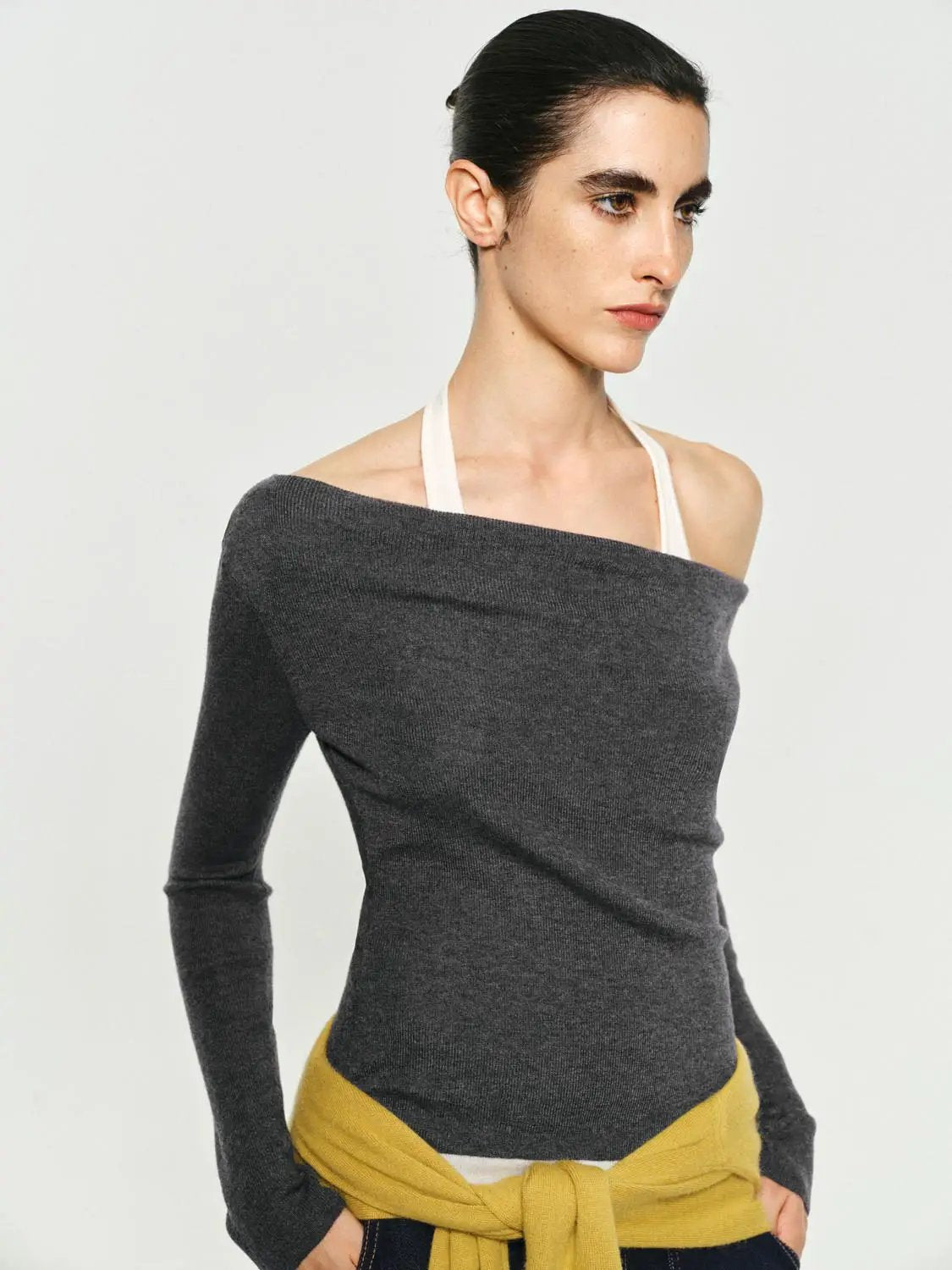 Fitted charcoal gray knit top with boat neck and long sleeves; white halter strap visible.