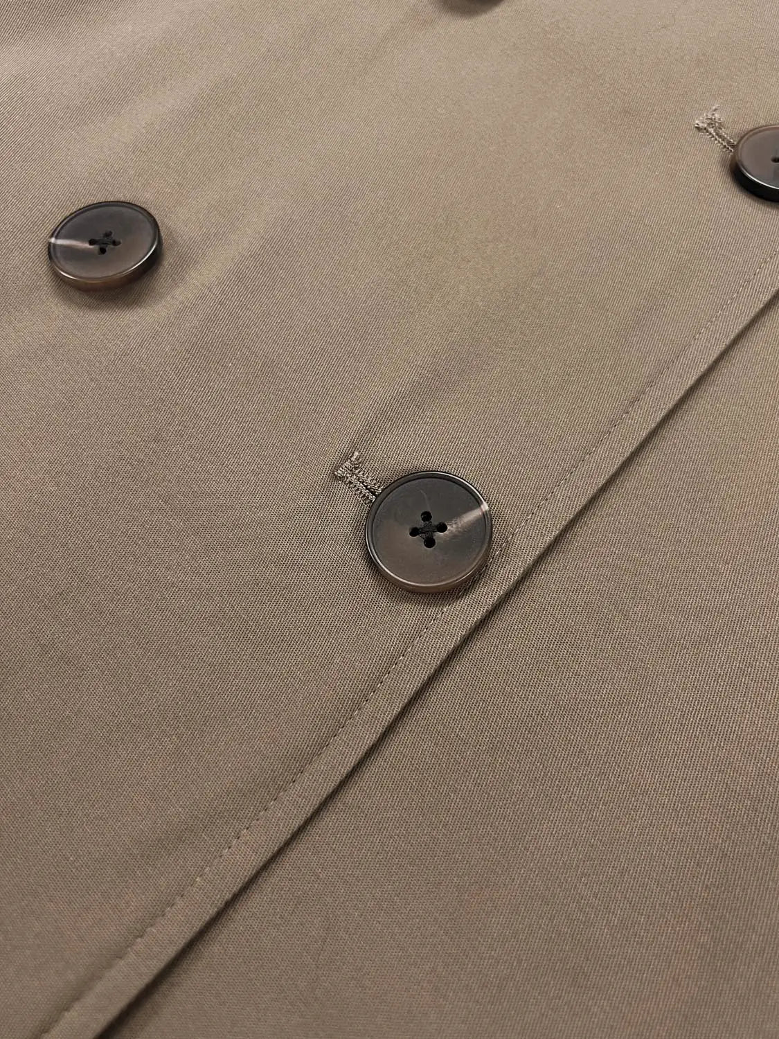 Trench coat close-up in tan beige fabric with dark brown buttons