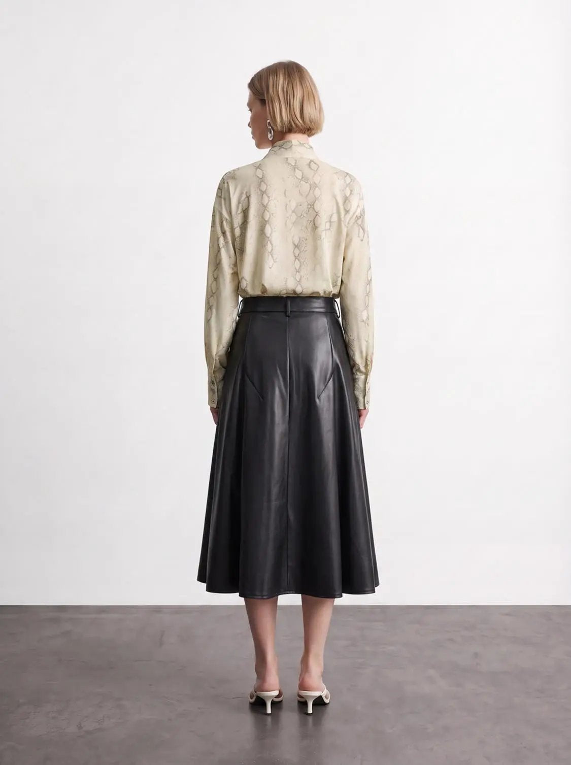 Pleated vegan leather A-line skirt by Urban Revivo Fashion in black; beige snake-print blouse shown.
