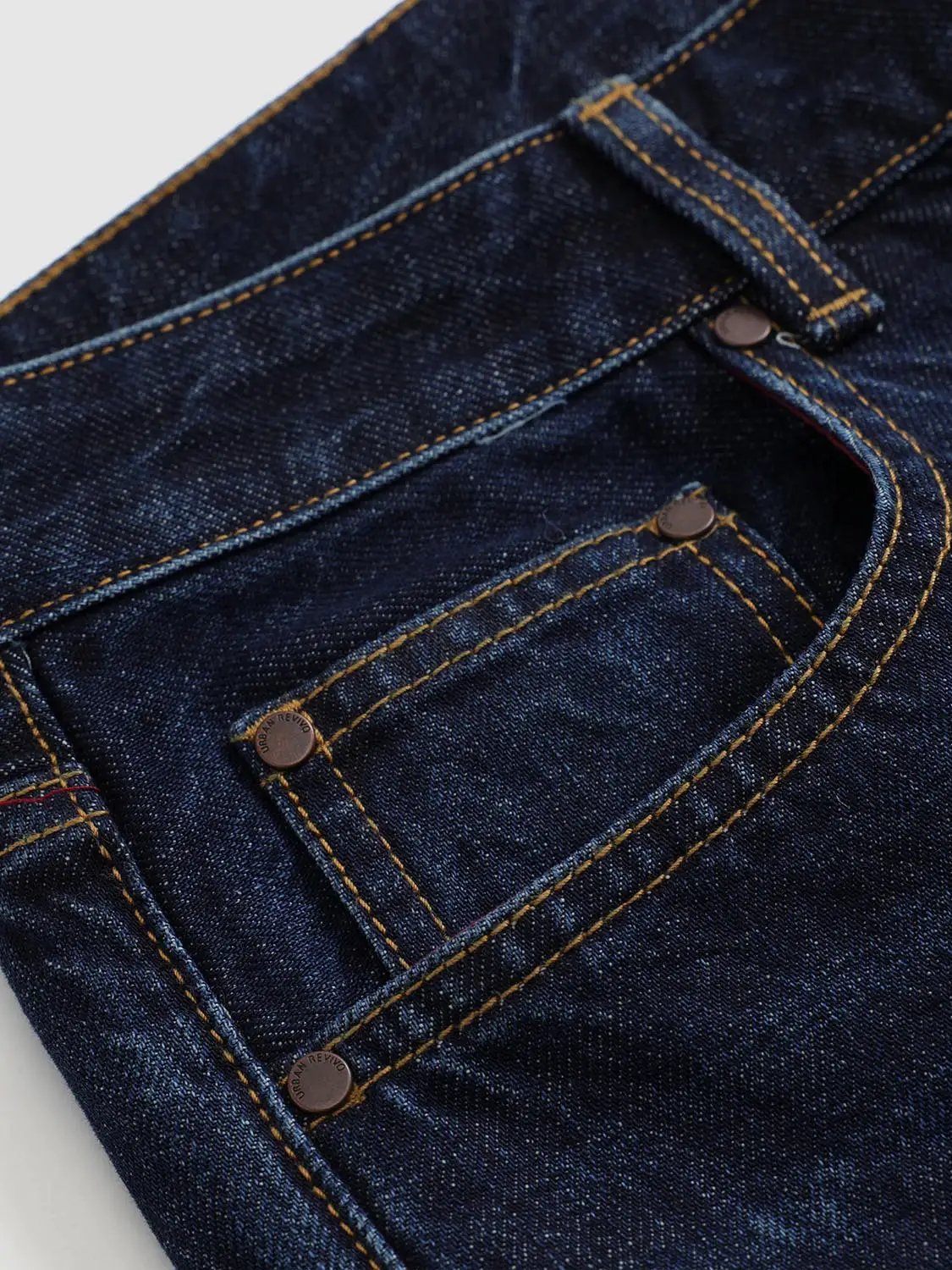 Urban Revivo jeans, dark indigo denim with copper rivets and yellow topstitching, pocket close-up.