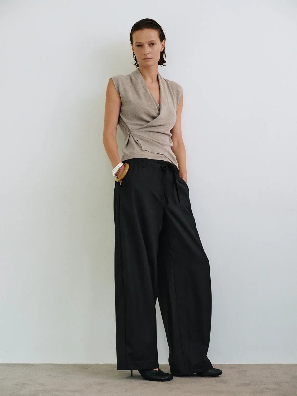 Beige sleeveless wrap-front knit top with collar, paired with black wide-leg pants