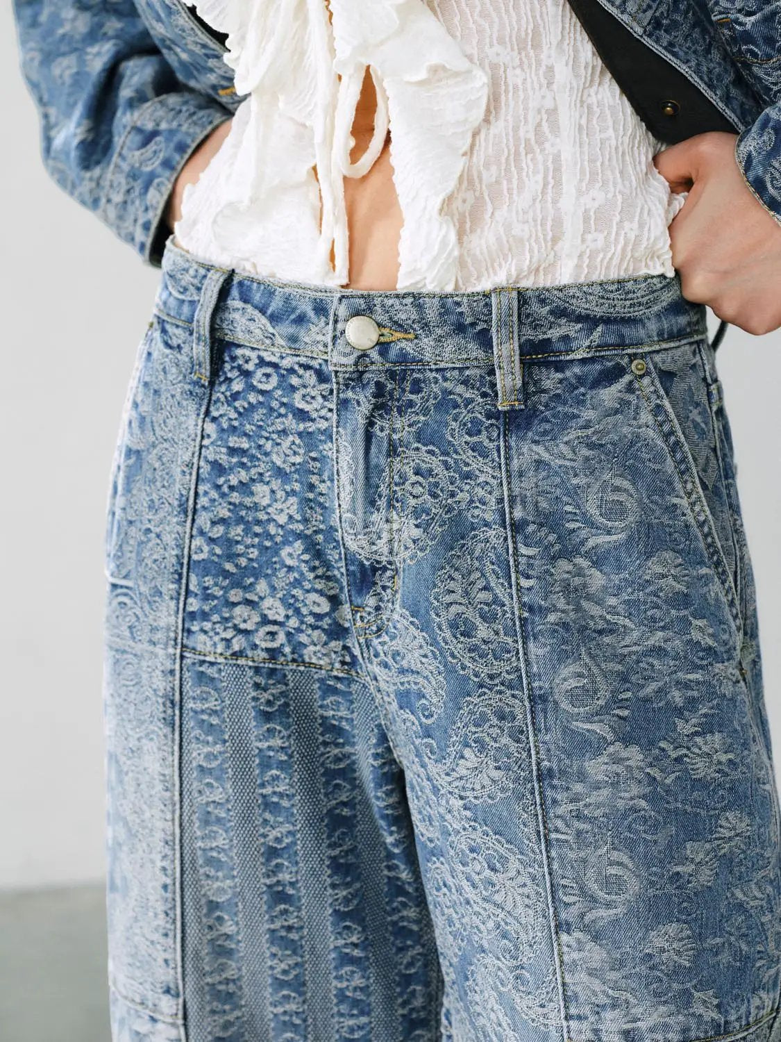 Jeans with blue denim fabric featuring floral lace pattern and front metal button.