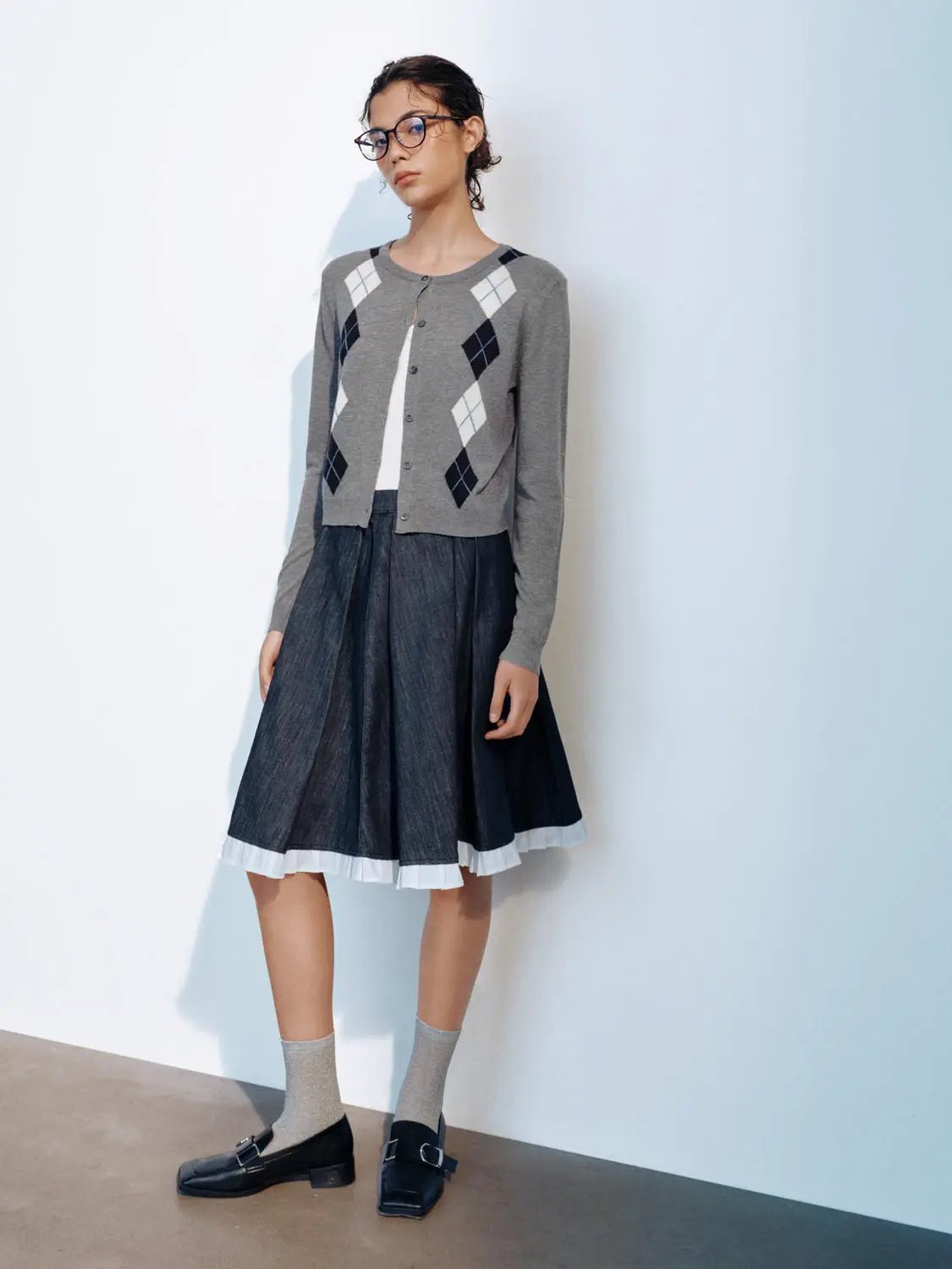 Knit cardigan in gray with white and navy argyle diamonds; button-front, paired with a dark midi skirt.