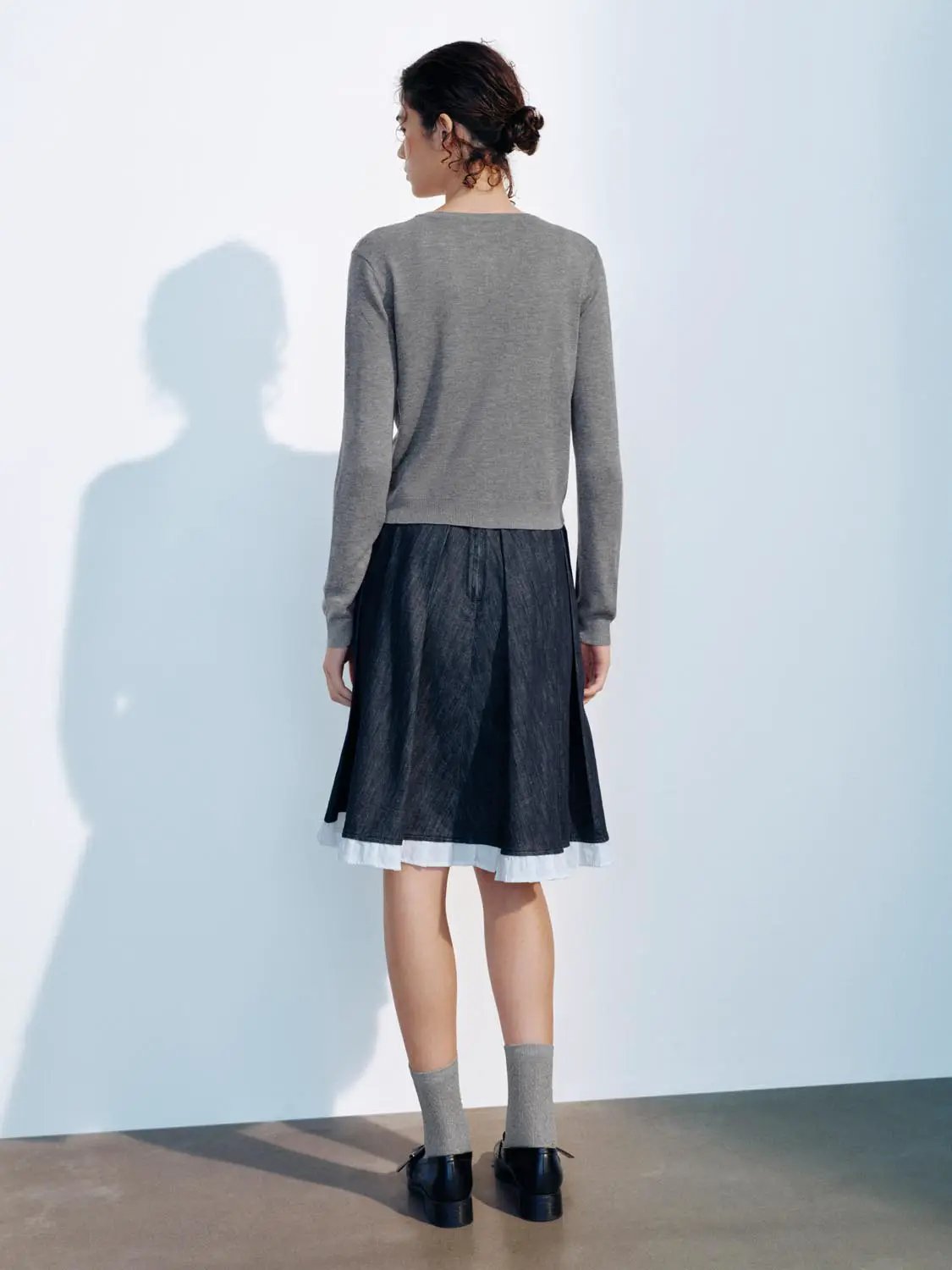 Knitted cardigan in gray worn by model with a layered dark skirt.