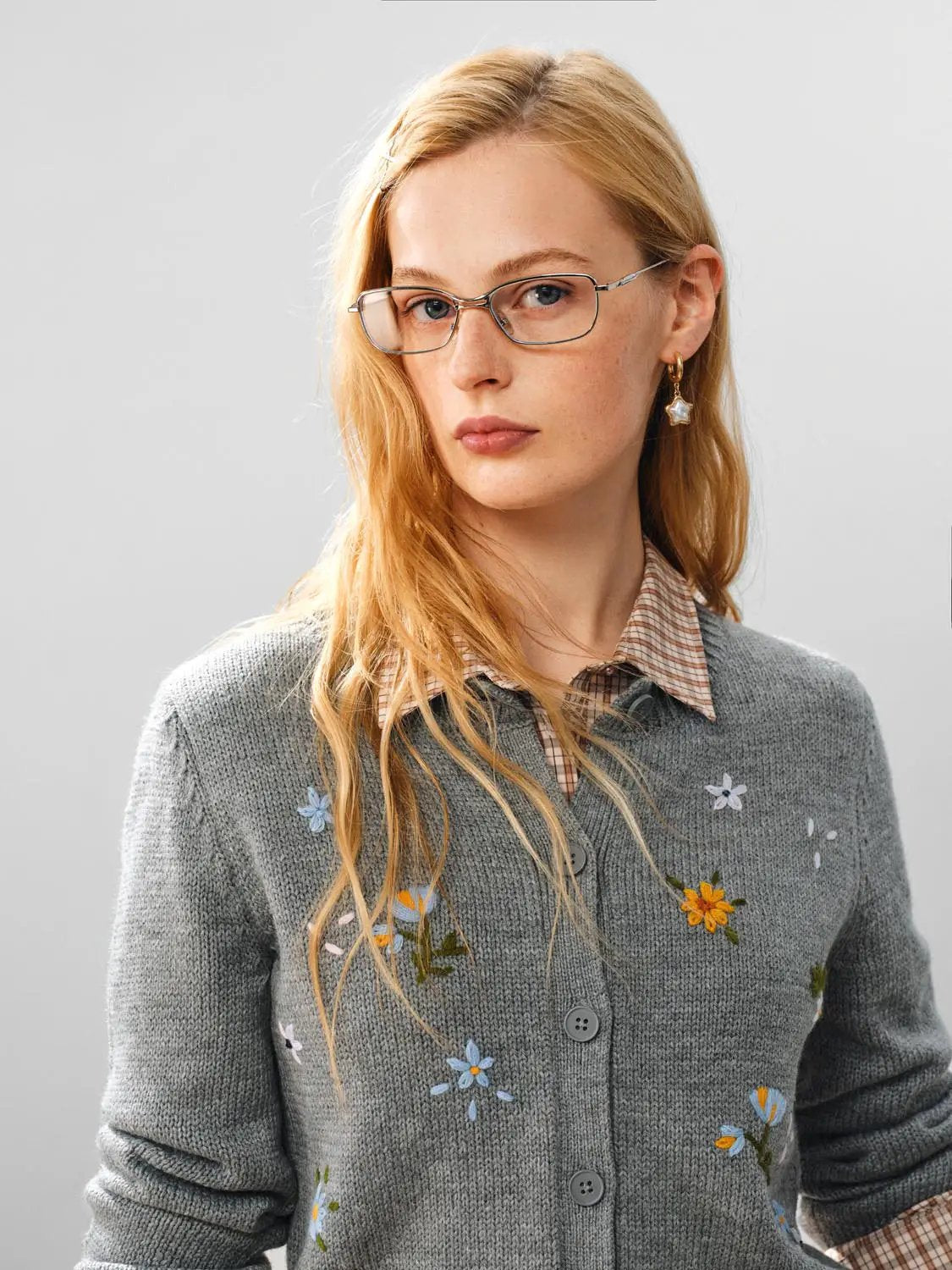 Knitted cardigan in gray with colorful floral embroidery, layered over a plaid shirt.
