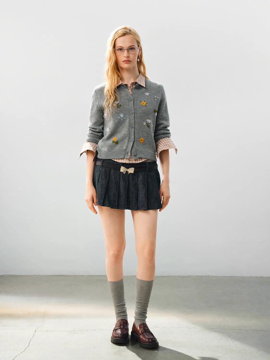 Knitted cardigan in gray with floral embroidery, layered over a check shirt and pleated mini skirt