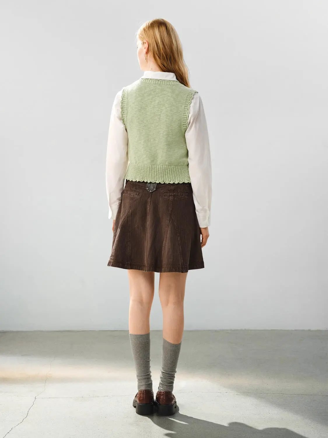 Floral ruffle tie V-neck sleeveless cotton vest; light green knit with ribbed hem worn over white shirt and brown skirt