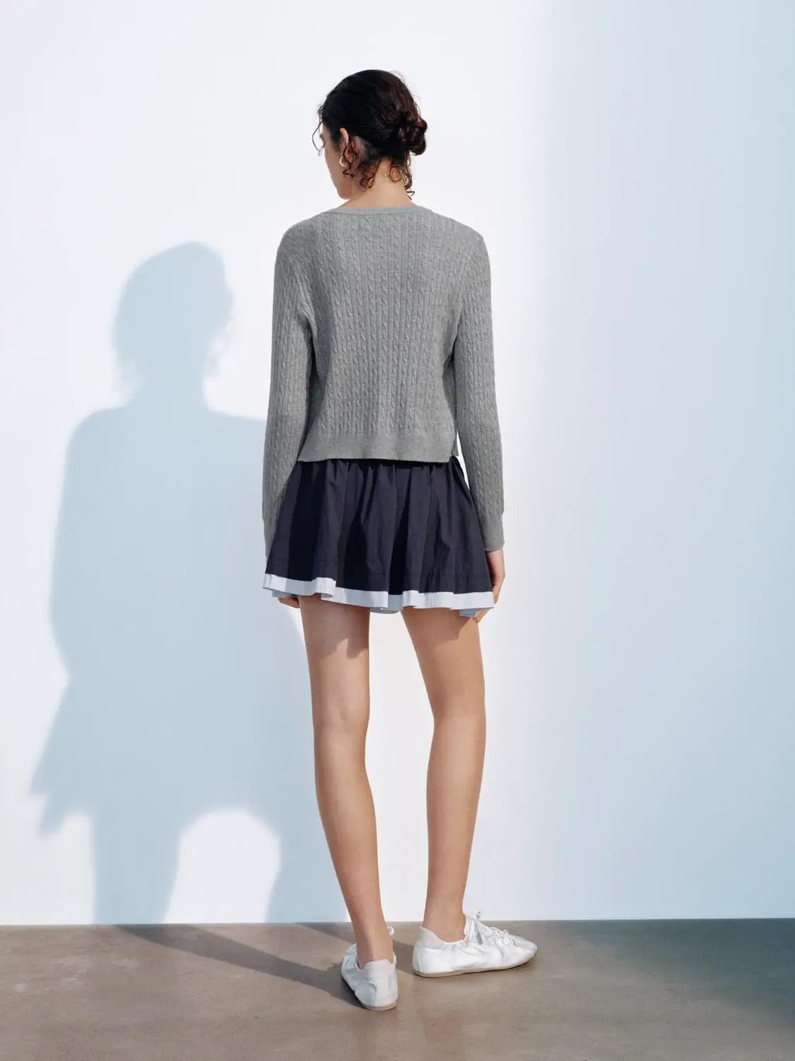 Grey knitted cardigan from Urban Revivo Fashion; back view, paired with a navy skirt with white hem.