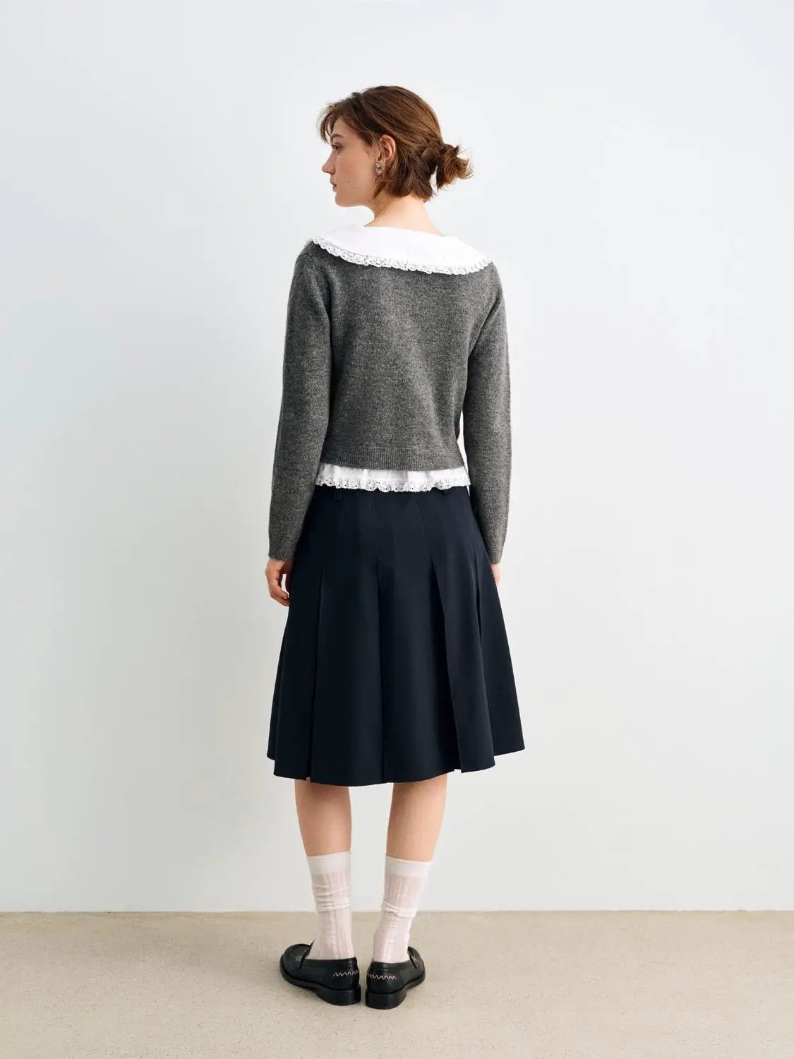 Knitted cardigan in grey with white lace collar and hem, paired with a navy pleated skirt