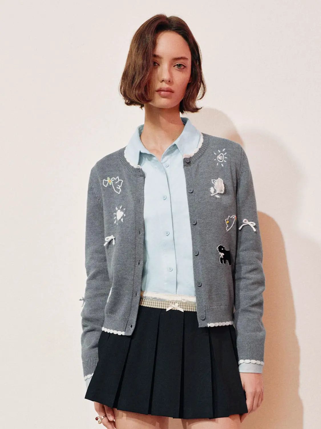Graphic long sleeve ribbed knit cardigan in grey with white trim and colorful embroidered patches.