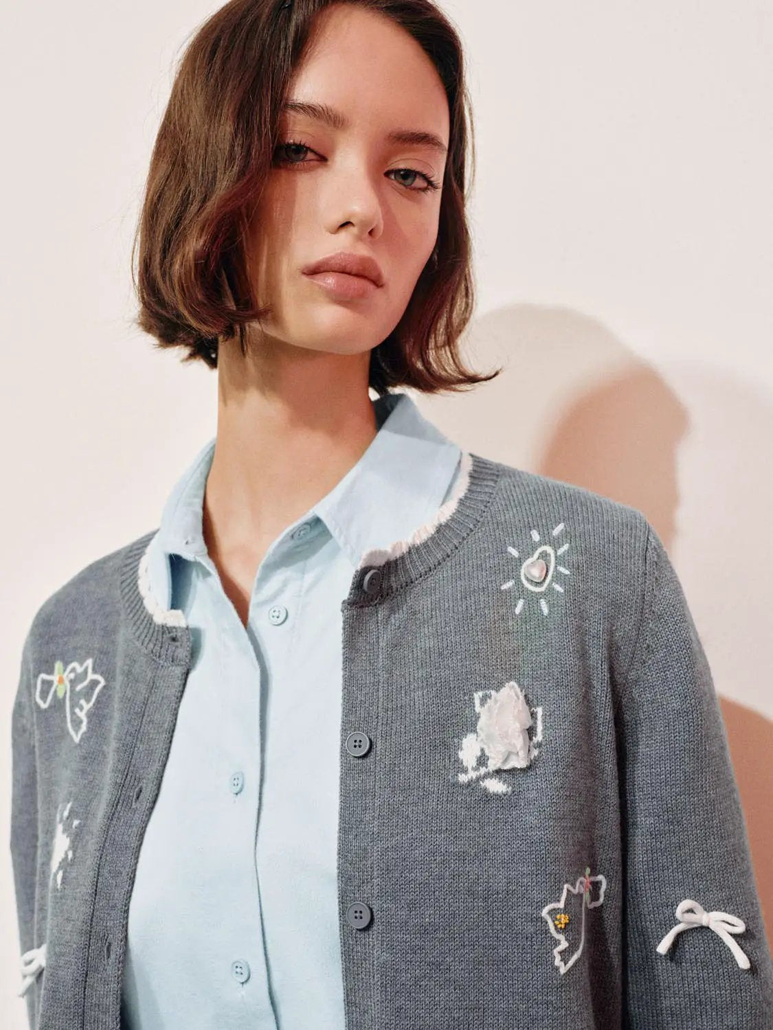 Graphic long sleeve ribbed knit cardigan in grey with embroidered patches, worn over a blue shirt by Urban Revivo.